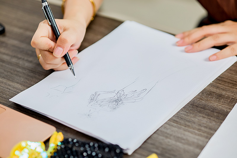 Croquis de couture dessiné à la main par un designer sur un bureau à côté de matériaux de perlage