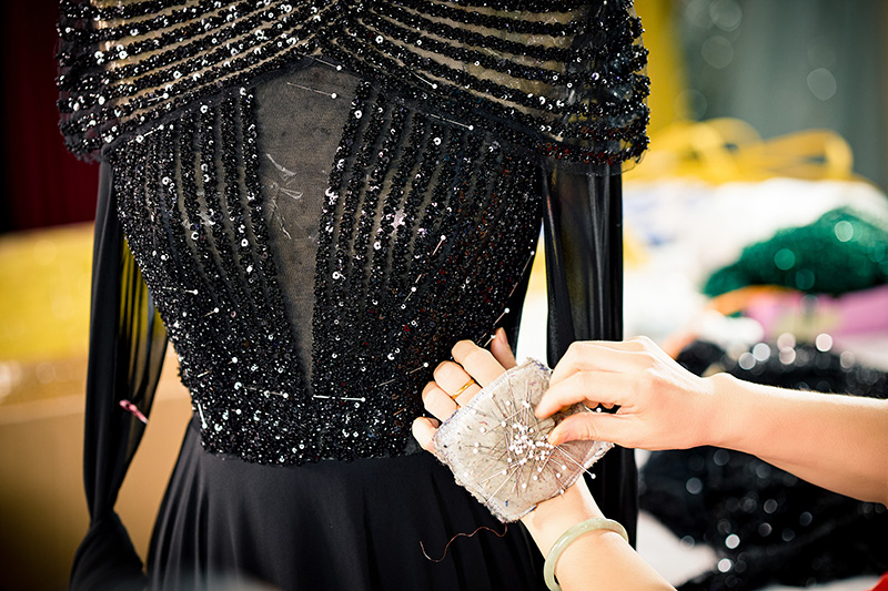 Une ouvrière épinglant et fixant un ornement à paillettes sur le buste d'une robe noire